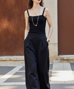Photograph of a slender woman with curly hair wearing a black cap tank top high waisted pants and sunglasses
