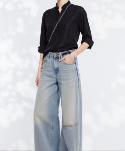 Photograph of a slender woman with light skin wearing a black blouse high waisted light blue jeans black sunglasses and sandals
