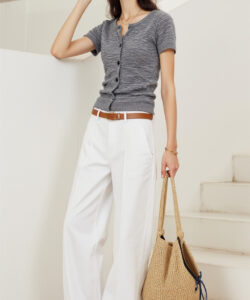 Photograph of a slender woman with long brown hair wearing a grey t shirt white pants and a wicker bag