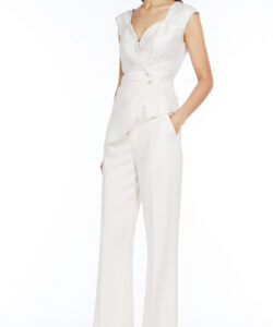 Photograph of a slender woman with long brown hair wearing a white sleeveless v neck romper and high waisted wide leg pants