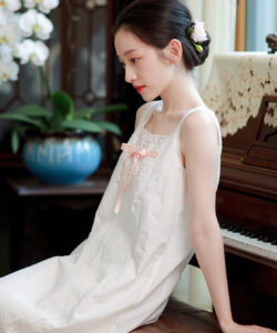 Photograph of a slim asian girl in a white sleeveless dress seated on a piano bench next to a blue vase
