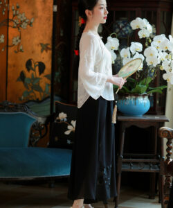 Photograph of a slim fair skinned asian woman in a white blouse and black skirt holding an orchid fan in a traditional ornate room