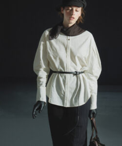 Photograph of a slim fair skinned woman in a white pinstriped blouse black skirt gloves and hat holding a bag