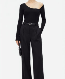 Photograph of a slim fair skinned woman with dark hair in a bun wearing a black off shoulder top and high waisted pants