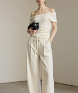 Photograph of a slim fair skinned woman with straight brown hair in a beige off shoulder top and matching wide legged pants