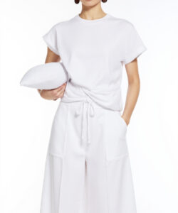 Photograph of a slim light skinned asian woman in a white short sleeve wrap front top and matching skirt holding a white pillow