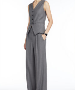 Photograph of a slim light skinned woman in a sleeveless grey vest and matching high waisted trousers standing against a plain white background