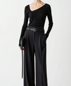 Photograph of a slim light skinned woman with straight dark hair wearing a black long sleeved top and high waisted black pants