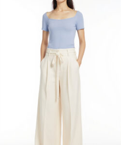 Photograph of a slim woman in a light blue top cream high waisted wide leg pants beige hat black sandals