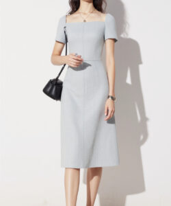 Photograph of a slim woman with glasses wearing a light blue off the shoulder dress standing against a plain white background