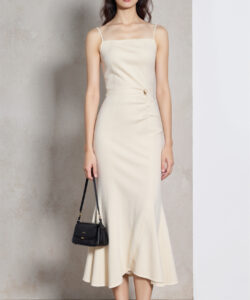 Photograph of a slim young asian woman in a cream sleeveless knee length dress holding a small black handbag