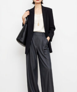 Photograph of a stylish light skinned woman with short black hair wearing a black blazer white blouse and gray high waisted pants