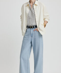 Photograph of a stylish woman in a cream hat white shirt zigzag pattern shirt light blue wide leg pants and black boots