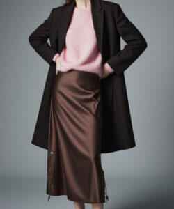 Photograph of a stylish woman in a pink sweater brown satin skirt black coat and black shoes