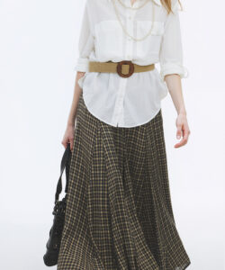 Photograph of a tall slender red haired woman in a white blouse plaid skirt tan belt carrying a black handbag