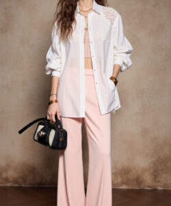 Photograph of a tall slender woman with long wavy brown hair wearing a white blouse and pink wide leg pants