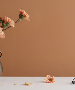 Photograph-of-a-vase-with-pink-flowers-on-a-white-surface-glasses-and-petals-scattered-against-a-muted-brown-background