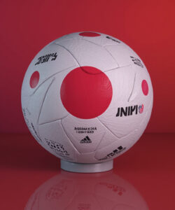 Photograph-of-a-white-Adidas-ball-with-red-Japan-logo-set-against-a-gradient-red-background-on-a-reflective-surface