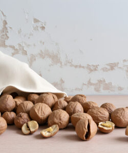 Photograph-of-a-white-cloth-bag-spilling-unshelled-walnuts-onto-a-light-wooden-surface-against-a-distressed-white-wall