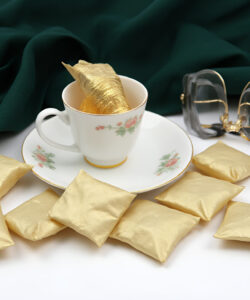 Photograph-of-a-white-teacup-with-floral-design-green-cloth-background-gold-tea-bag-and-gold-sugar-cubes