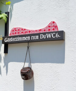 Photograph-of-a-white-wall-with-a-black-sign-reading-Gastezimmer-111-DWVCG-featuring-a-red-and-white-pattern