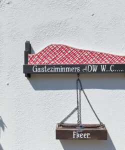 Photograph-of-a-white-wall-with-a-wooden-sign-reading-Gastzeimmer-DW-Free-and-ivy-on-the-left
