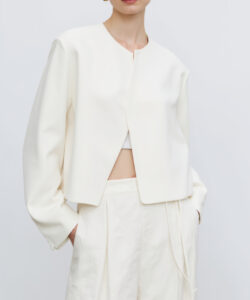 Photograph of a woman with dark hair fair skin wearing a white cropped jacket and matching high waisted pants minimalist background