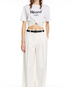 Photograph of a woman with wavy brown hair wearing black sunglasses a white crop top and high waisted white pants