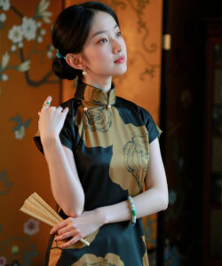 Photograph of a young asian woman in a traditional black and gold qipao holding a fan in an ornate room