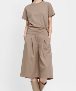 Photograph of a young asian woman in beige short sleeve top and matching skirt beige knee high boots against white background
