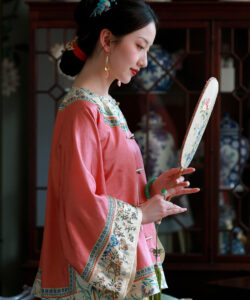 Photograph of a young asian woman in traditional chinese attire holding a fan against a background of blue porcelain