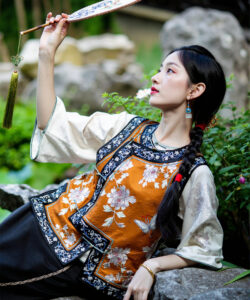 Photograph of a young asian woman in traditional chinese attire holding a fan set against a lush garden backdrop