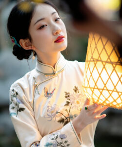 Photograph of a young asian woman in traditional chinese dress holding a glowing lantern against a blurred natural background