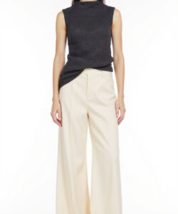 Photograph of a young woman in a sleeveless dark knit top and high waisted cream colored wide leg pants standing against a white background