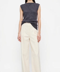 Photograph of a young woman in a sleeveless grey top and cream wide leg pants standing against a plain white background