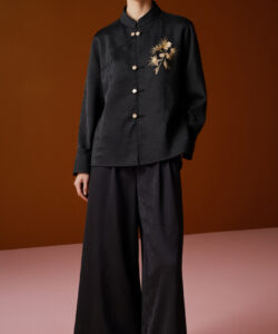 Photograph of an asian woman in black satin jacket and matching wide leg pants against a brown and pink gradient background