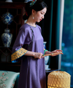 Photograph of an east asian woman in a purple cheongsam pouring tea with traditional decor and a lantern in background