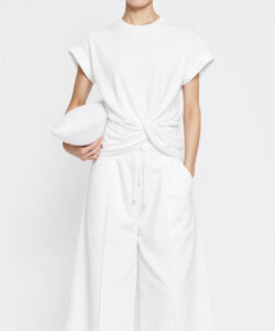 Photograph of an east asian woman in a white sleeveless tunic and matching pants holding a white hat