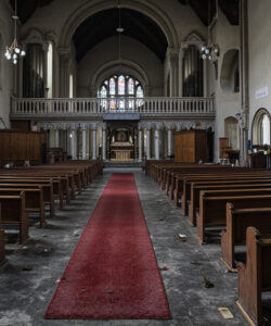 Photograph-of-an-empty-dimly-lit-church-with-red-carpet-wooden-pews-gothic-architecture-and-religious-paintings-on-the-walls