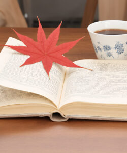 Photograph-of-an-open-book-with-a-red-maple-leaf-on-it-a-white-teacup-with-blue-flowers-and-a-wooden-table