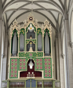 Photograph-of-an-ornate-Gothic-style-pipe-organ-in-a-grand-cathedral-featuring-intricate-carvings-vibrant-green-and-red-details