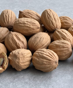 Photograph-of-brown-wrinkled-hazelnuts-scattered-on-a-grey-textured-surface-with-one-nut-cracked-open-revealing-its-interior