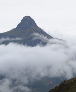 Photograph-of-two-hikers-on-a-mountain-slope-with-a-towering-mist-shrouded-peak-in-the-background-under-a-cloudy-sky