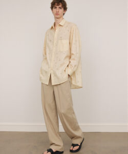 Caucasian Man In Beige Shirt And Pants Black Sandals Standing Against Plain
