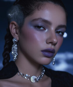 A Woman With Braided Hair Purple Eyeshadow Eyeshadow And Silver Jewelry Against A Dark