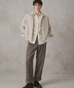 A Young Man With Curly Hair Wearing A A Beige Jacket Striped Shirt Brown Pants And