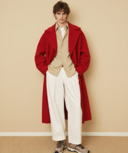 A Young Man With Curly Hair Wearing A A Red Coat Beige Shirt White Pants And