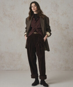 A Young Woman In A Brown Velvet Suit Suit Long Wavy Hair Standing Against A Textured