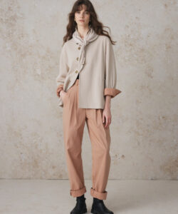A Young Woman With Wavy Brown Hair Wearing Wearing A Beige Coat Scarf Pink Pants And