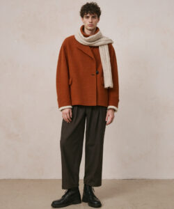 Curly Haired Man In An Oversized Rust Rust Orange Coat Beige Scarf Dark Pants